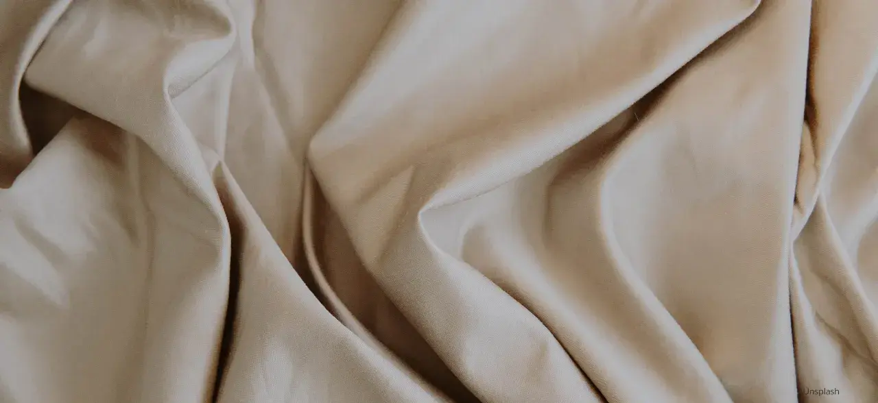 Sanfter, beige Stoff fällt in weichen Falten. Lyocell ist das, ein nachhaltiges Material, das sich so angenehm anfühlt.
