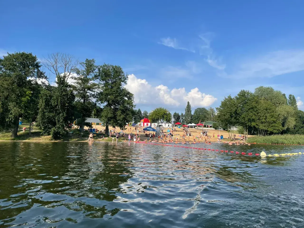 Słoneczny dzień nad jeziorem, pełnym ludzi kąpiących się i opalających. To jedne z fajnych miejsc nad wodą mazowieckie.