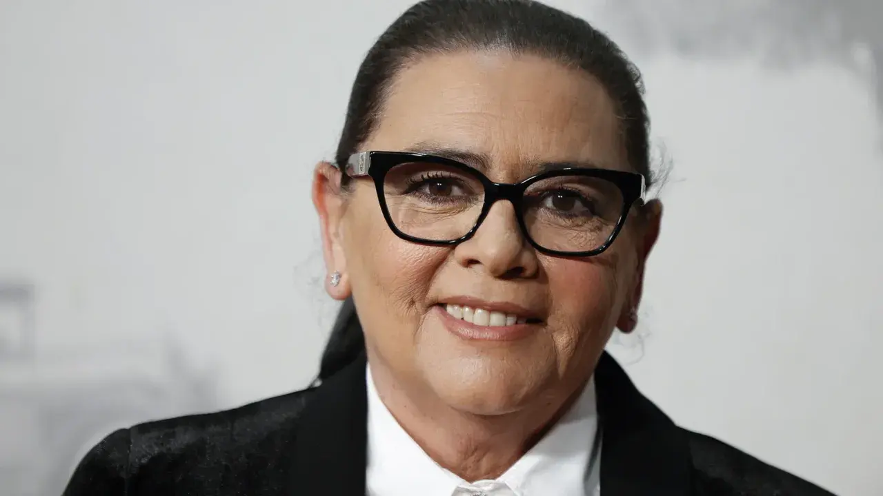 María del Monte, con gafas negras y una sonrisa amable, luce un traje elegante.