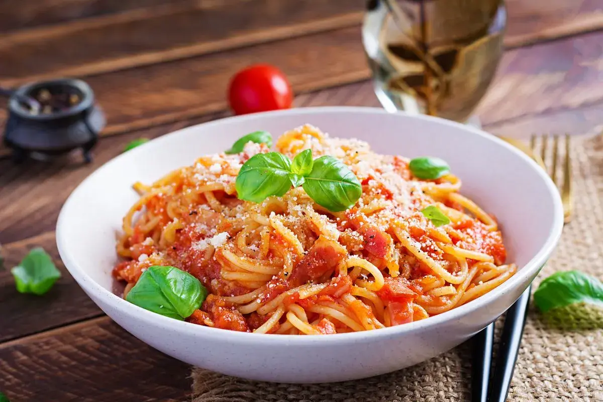 Un piatto di spaghetti alla corte d'assise, conditi con pomodoro fresco e basilico, spolverati di parmigiano.