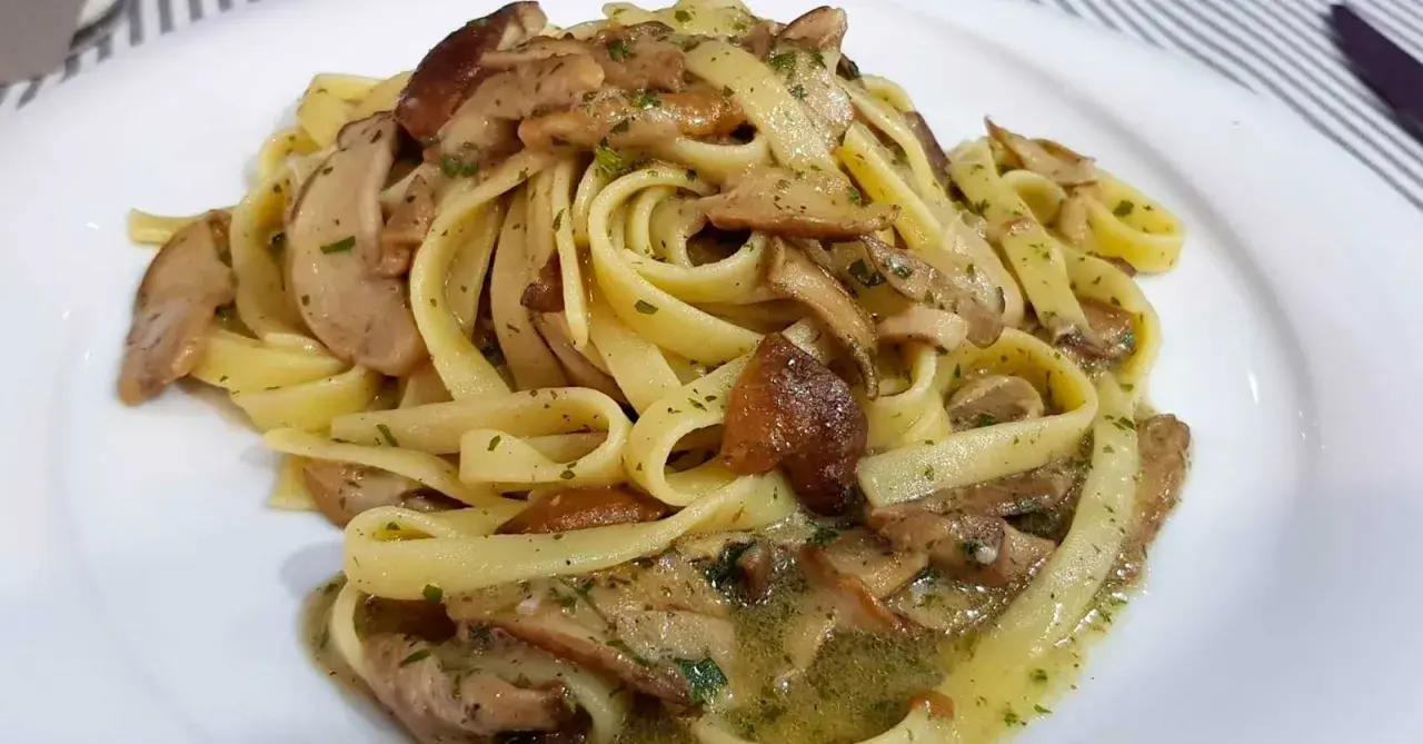 Un piatto invitante di tagliatelle ai porcini, condite con funghi freschi e prezzemolo tritato, su un piatto bianco.
