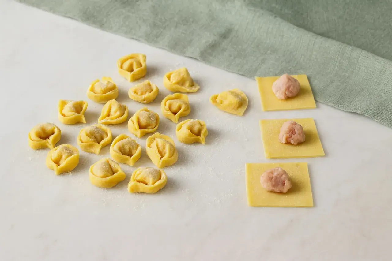Frische Tortellini und Teigquadrate mit Füllung auf Marmorplatte.
