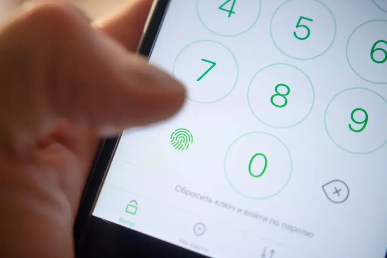 Zbliżenie na ekran telefonu z klawiaturą numeryczną, ikoną odcisku palca i palcem wskazującym.