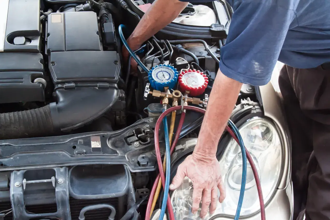 Mecánico realizando la tarea de cargar gas aire acondicionado en un coche, con manómetros y mangueras conectadas al motor.