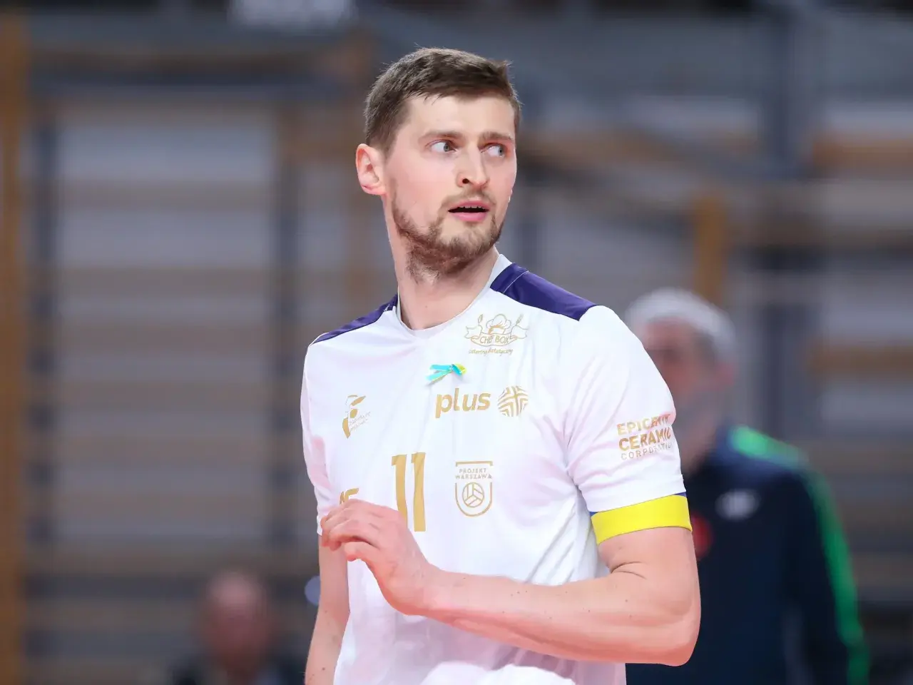 Piotr Nowakowski, siatkarz w białej koszulce z numerem 11, z uwagą obserwuje grę.