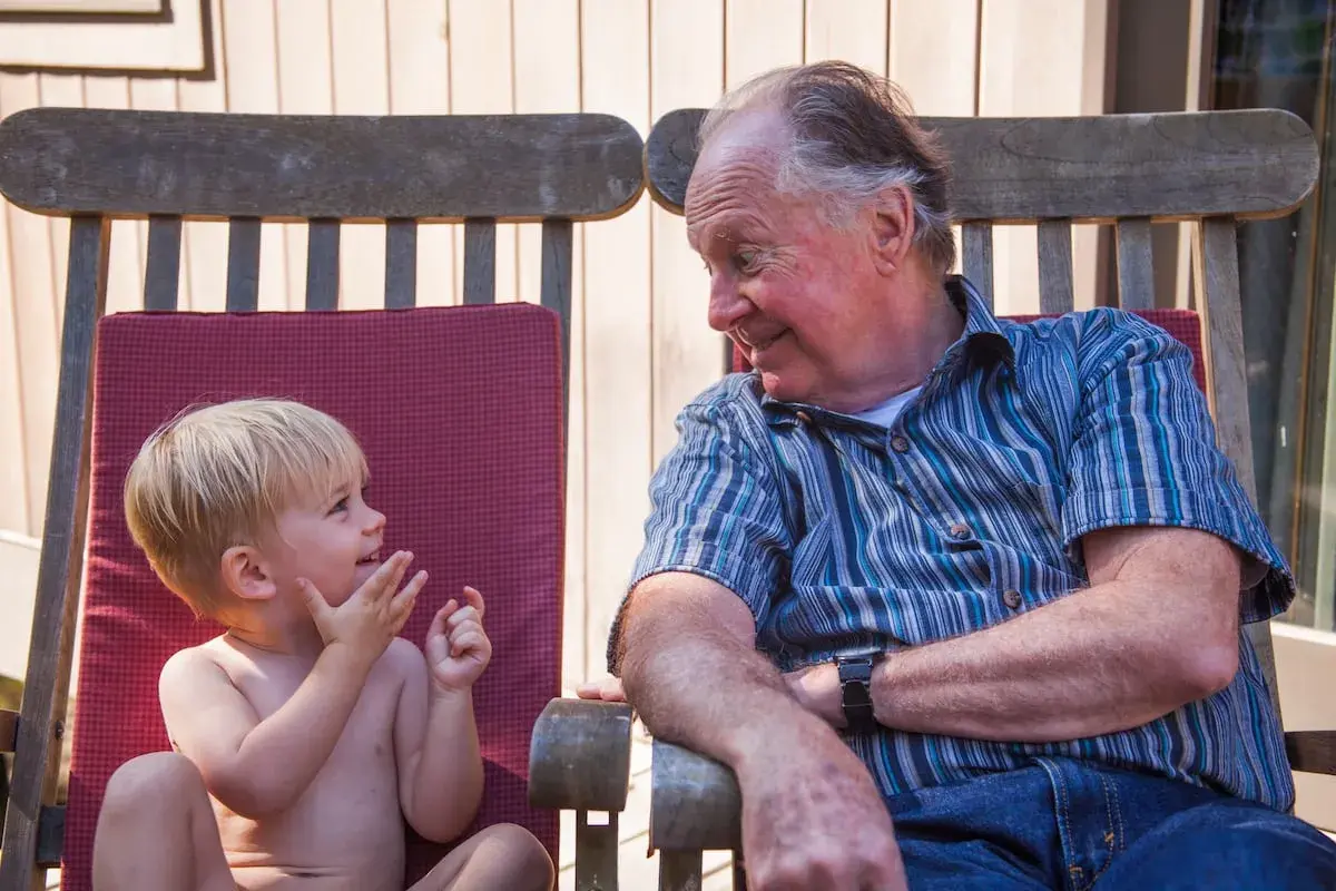 Un abuelo sonríe a su nieto, un momento tierno que los padres disfrutan al dejar a sus hijos con los abuelos.
