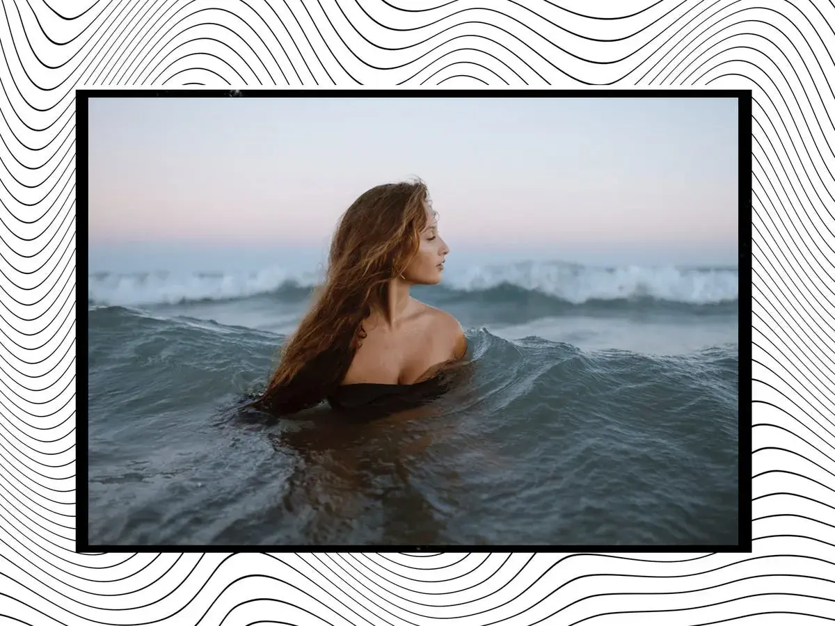 Mujer con cabello largo y ondulado se sumerge en el mar, rodeada de olas que parecen invitar a soñar con olas gigantes.
