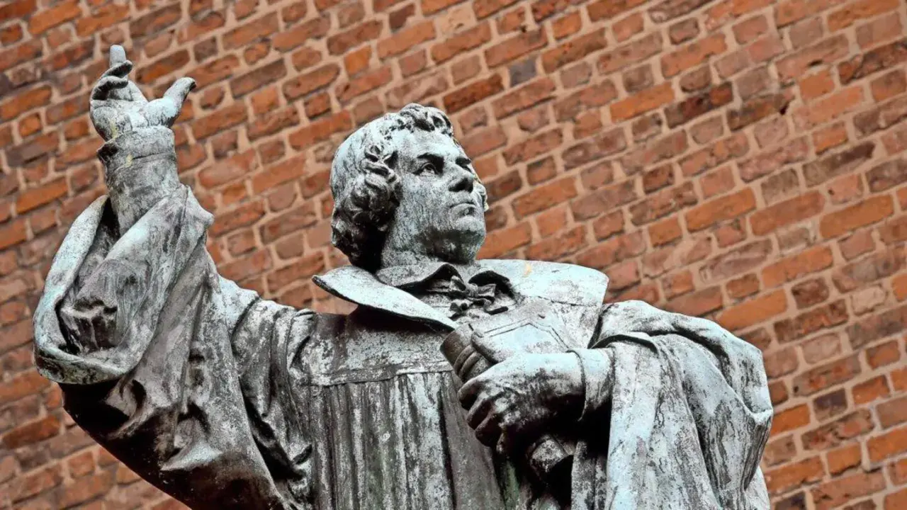 Statue eines Mannes mit Buch und erhobener Hand vor Ziegelwand. Ein Denkmal, das an den Reformationstag in Schleswig-Holstein erinnert.