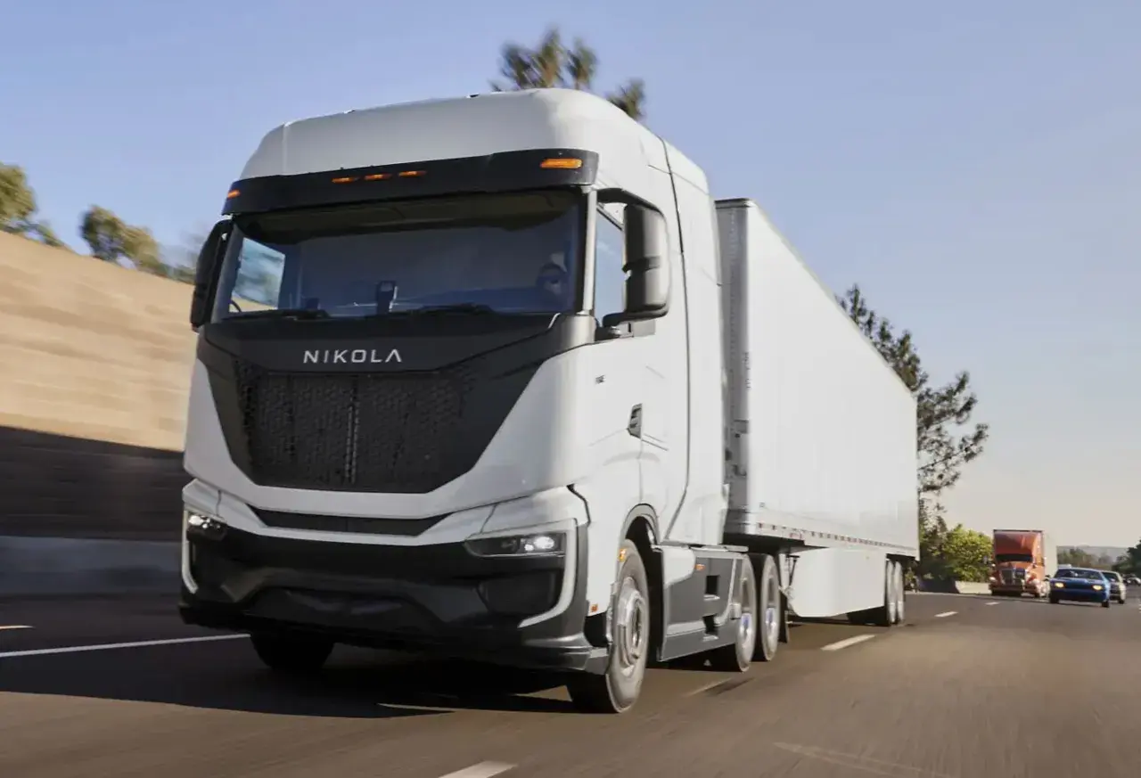Le Nikola One, un camion blanc futuriste, roule sur l'autoroute sous un ciel bleu clair.