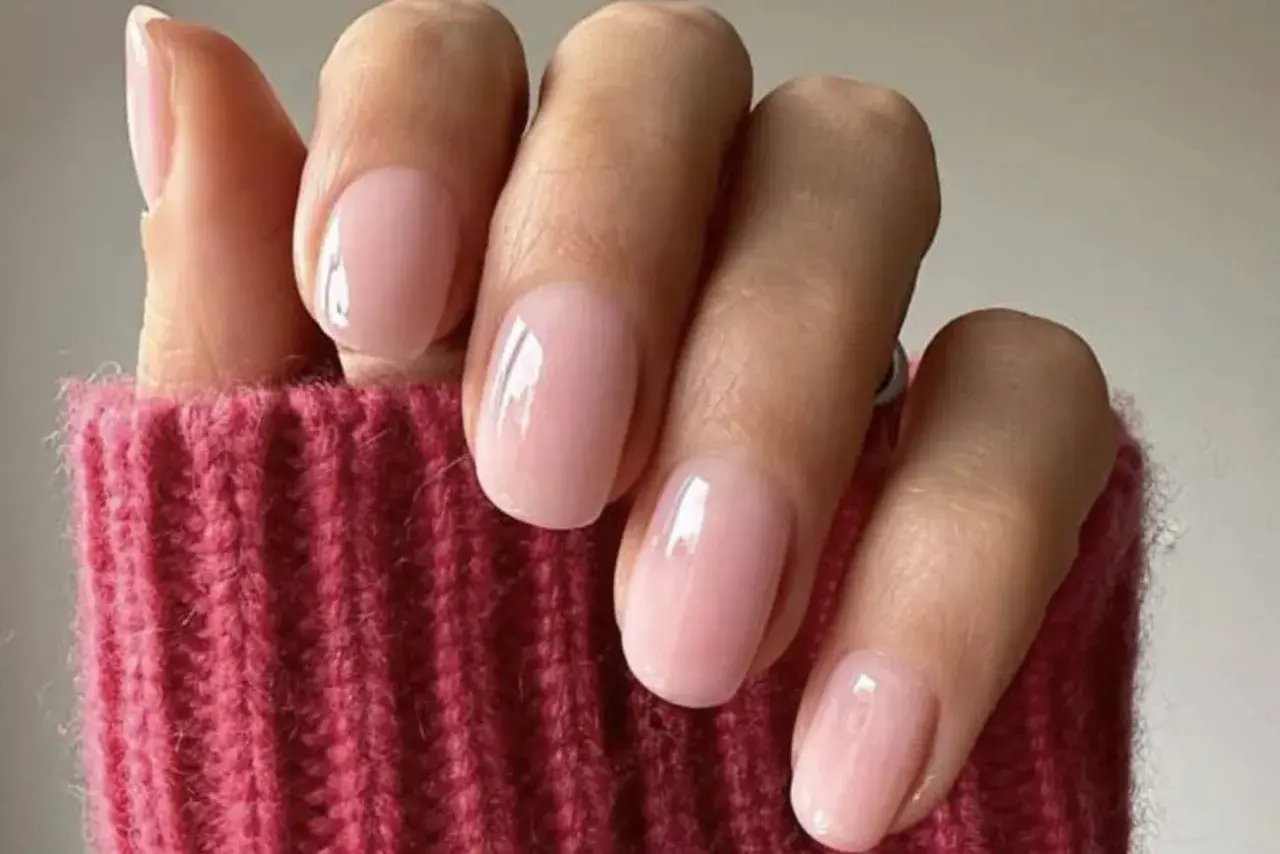 Delikatne, różowe paznokcie w stylu "soap nails" lśnią na tle grubego, różowego swetra.