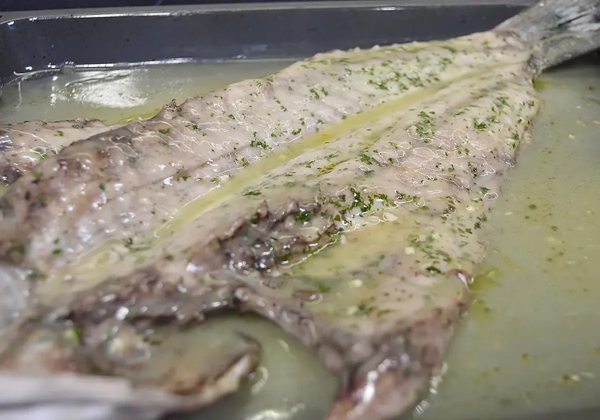 Lubina salvaje preparada en una bandeja con salsa de limón y hierbas, lista para cocinar.
