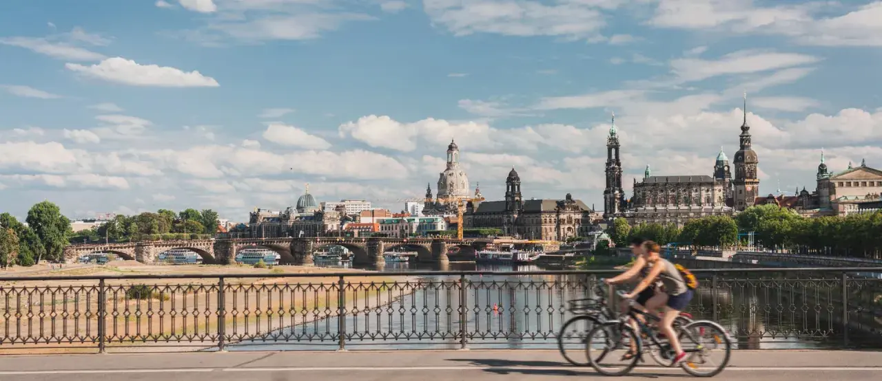 Two people enjoy bike tours in Germany, cycling across a bridge with a scenic view of Dresden's historic skyline.