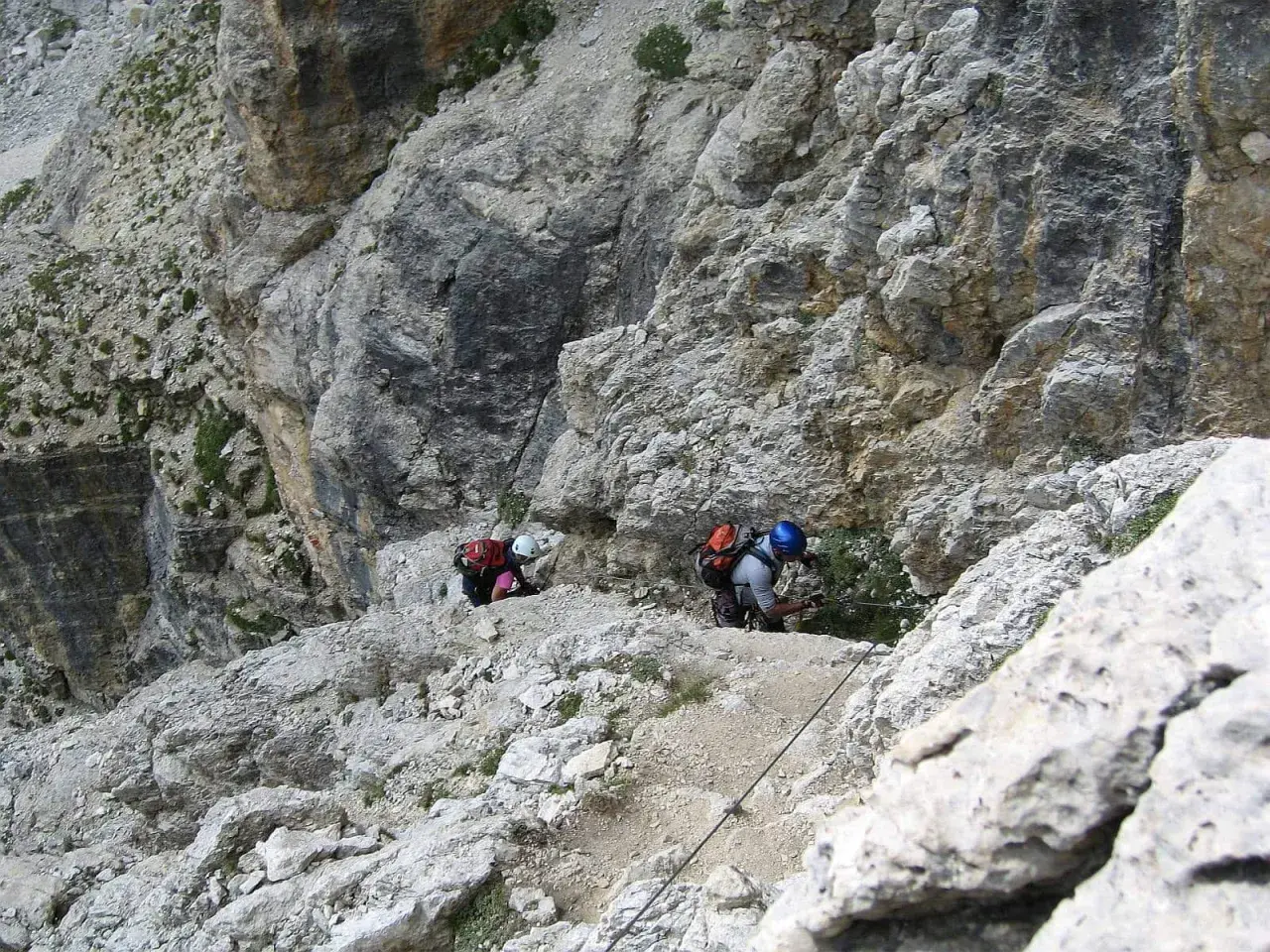 Dwóch wspinaczy pokonuje trudną trasę na ferratach w Dolomitach, korzystając z liny asekuracyjnej.