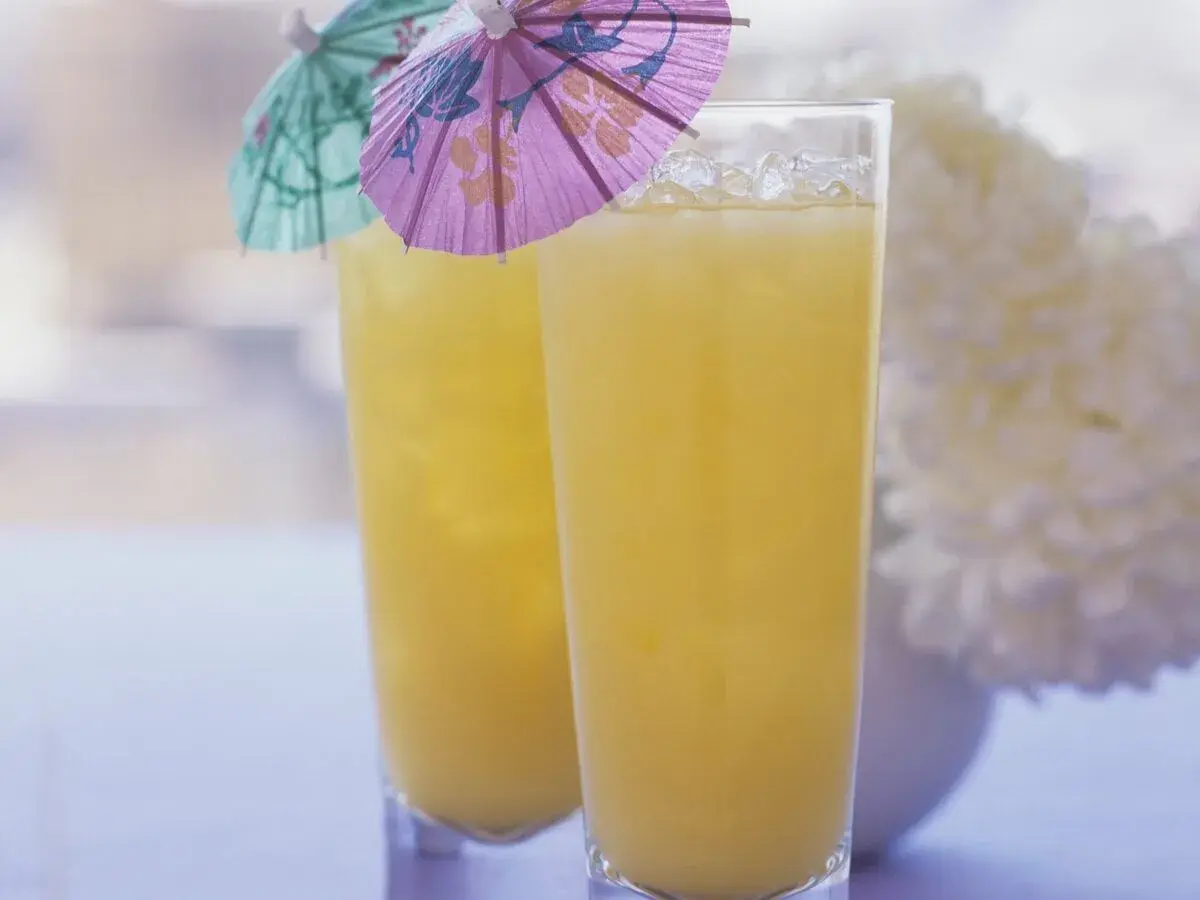 Zwei Gläser mit gelbem Saft und Eis, dekoriert mit kleinen bunten Schirmchen.