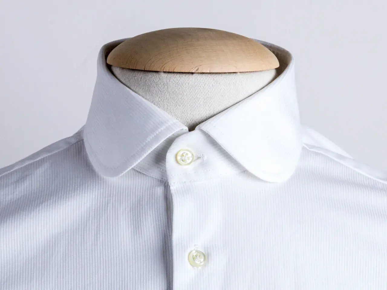 Dettaglio di una camicia bianca con colletto arrotondato, uno dei tanti tipi di colletto camicia, su un manichino.