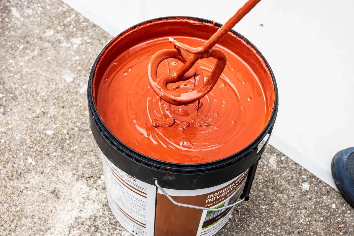 Mezclando pintura impermeabilizante naranja en un cubo. El tiempo secado pintura impermeabilizante es clave para un buen acabado.