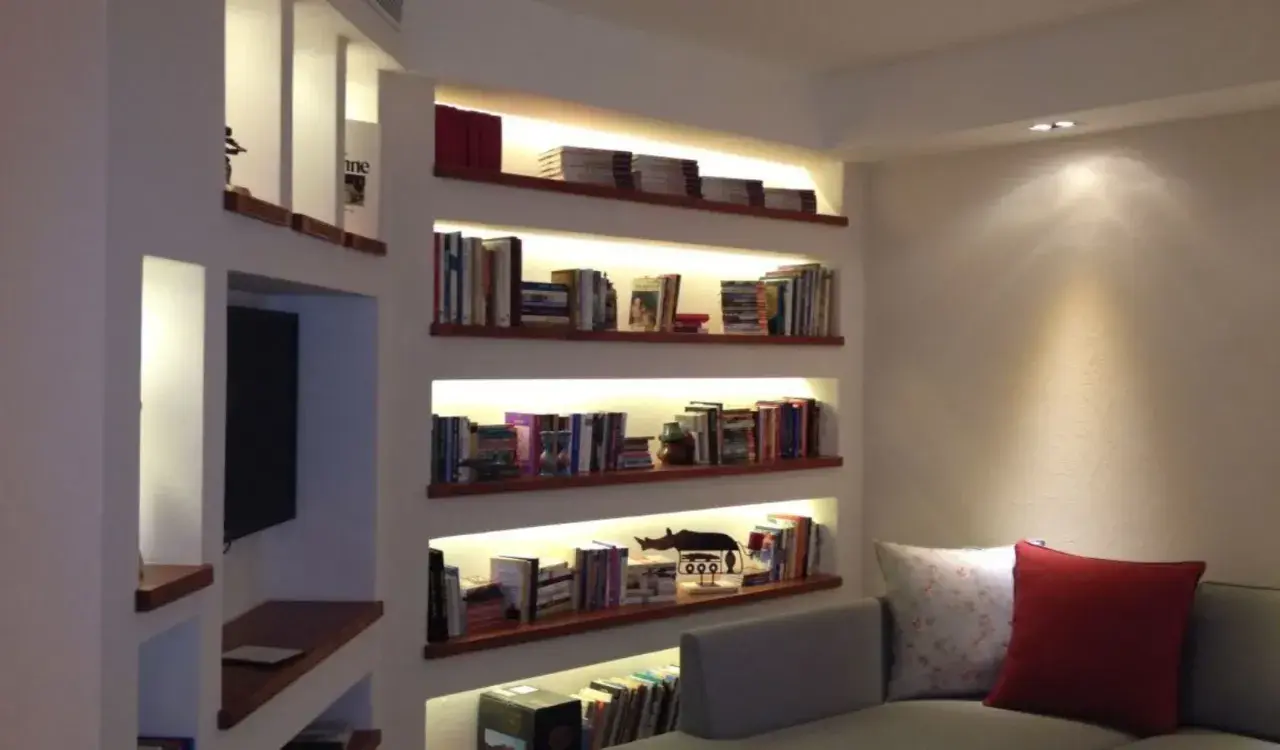 Libreria cartongesso angolare con illuminazione integrata, piena di libri e oggetti decorativi.