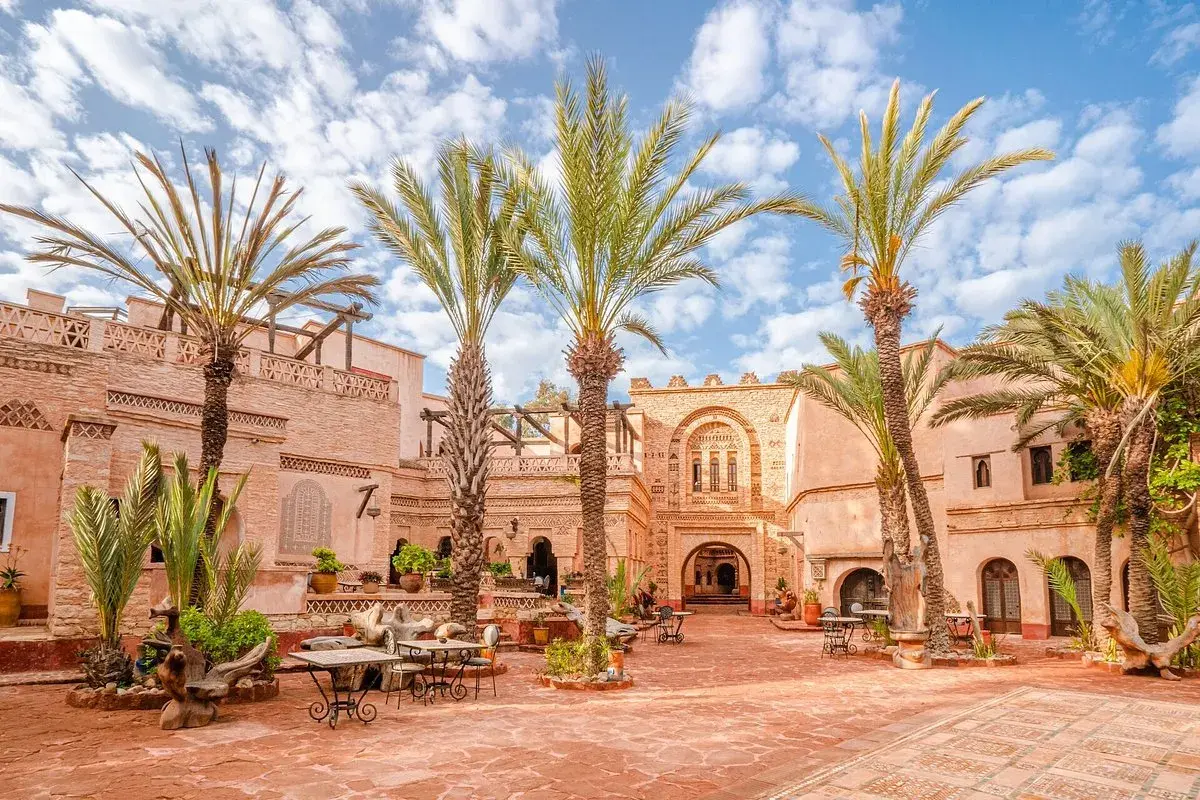 Sonniger Innenhof in der Agadir Altstadt mit Palmen, traditioneller Architektur und Sitzgelegenheiten im Freien.