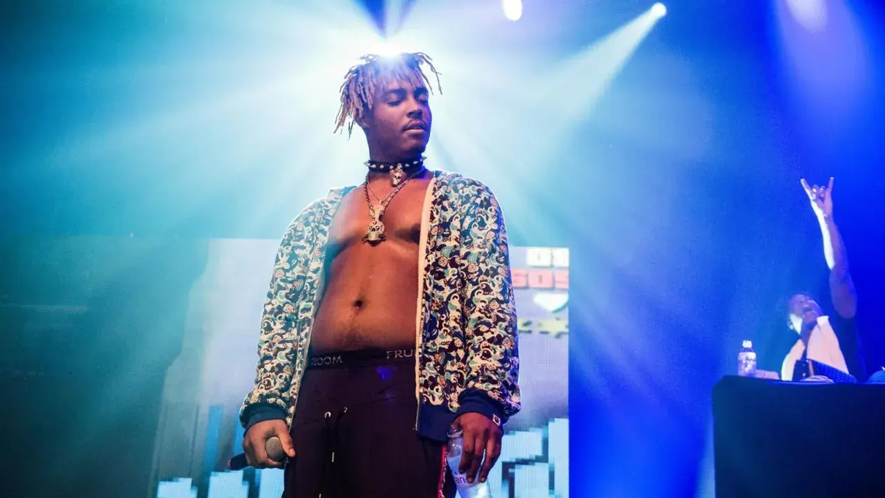 Juice WRLD on stage, a testament to his massive Juice WRLD Spotify streams. The artist, bathed in blue light, holds a microphone and a bottle.