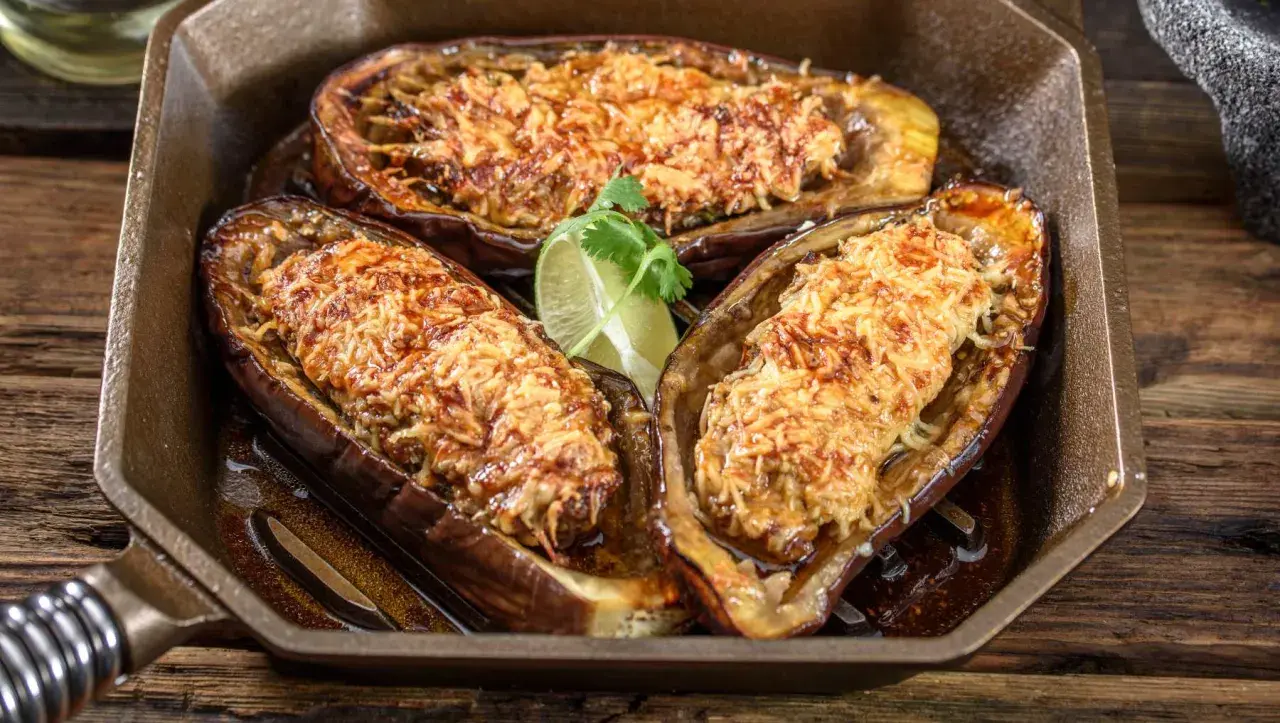 Berenjena airfryer rellena y gratinada, servida en una sartén de hierro fundido con un toque de lima.
