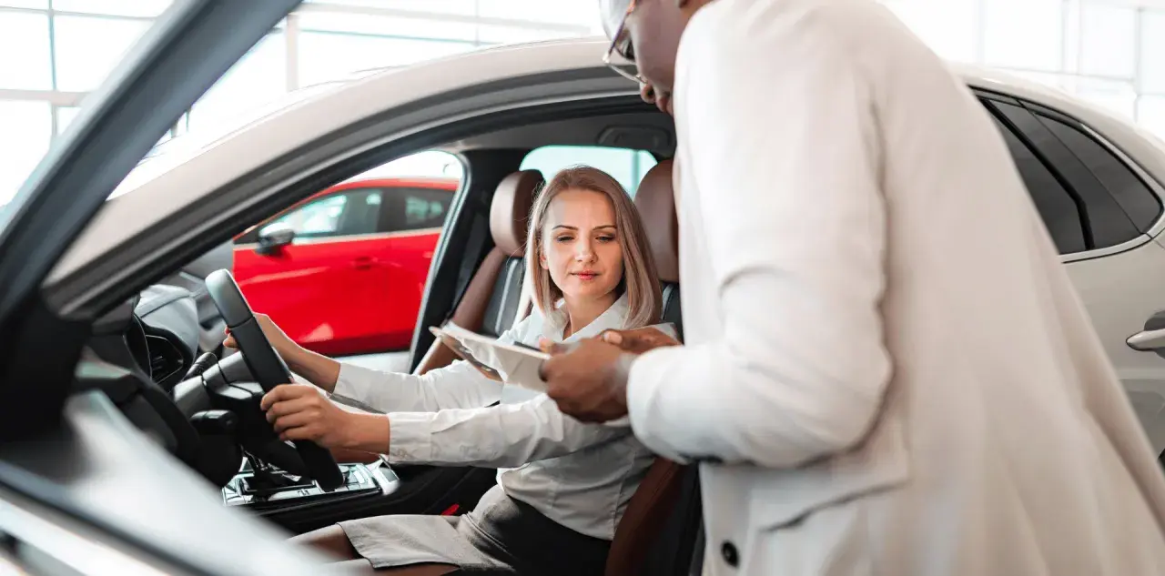 Kobieta za kierownicą nowego auta, sprzedawca omawia warunki fiat leasing.