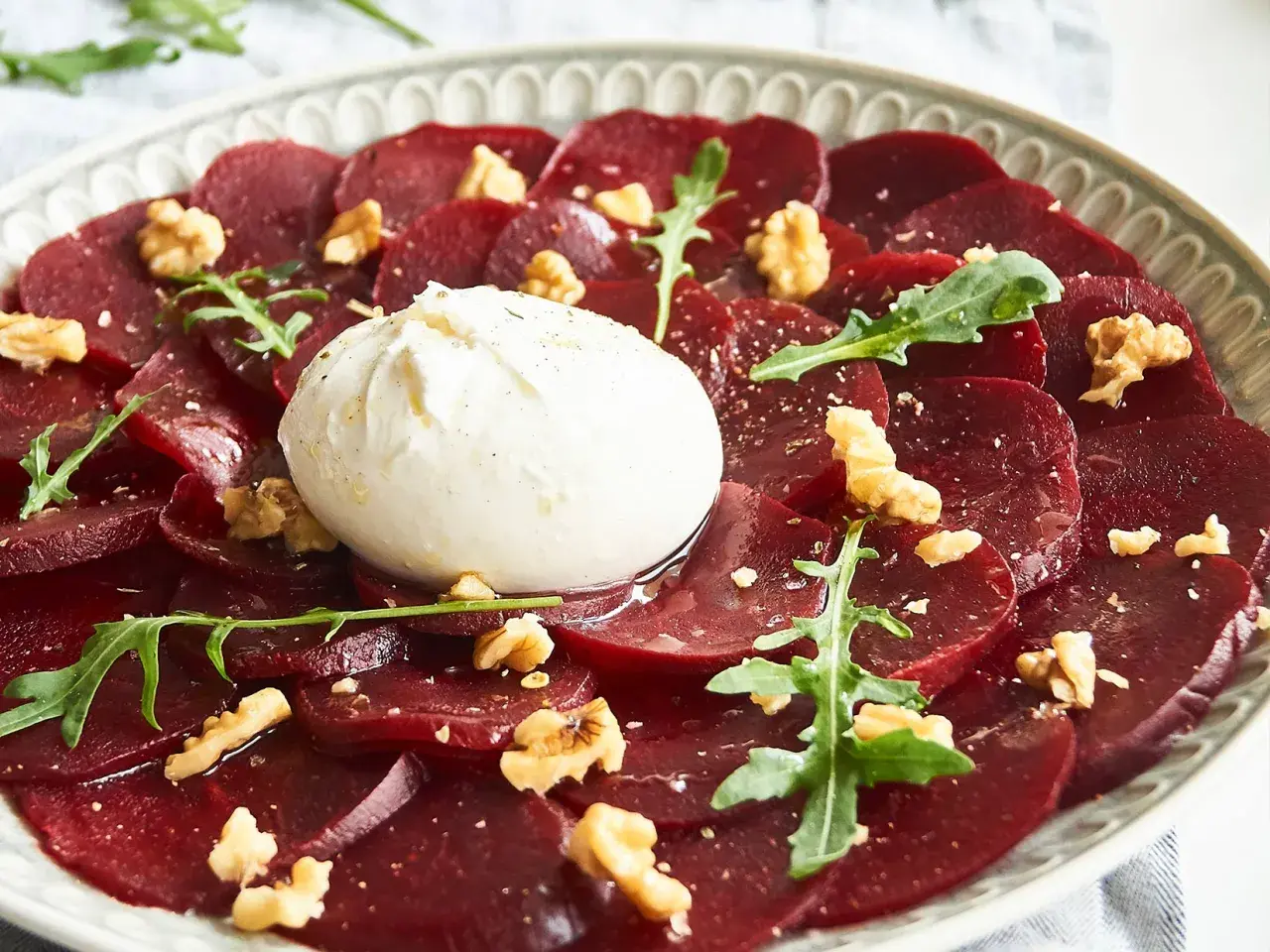 Rote Bete Carpaccio italienisch mit Burrata, Walnüssen und Rucola auf einem Teller.