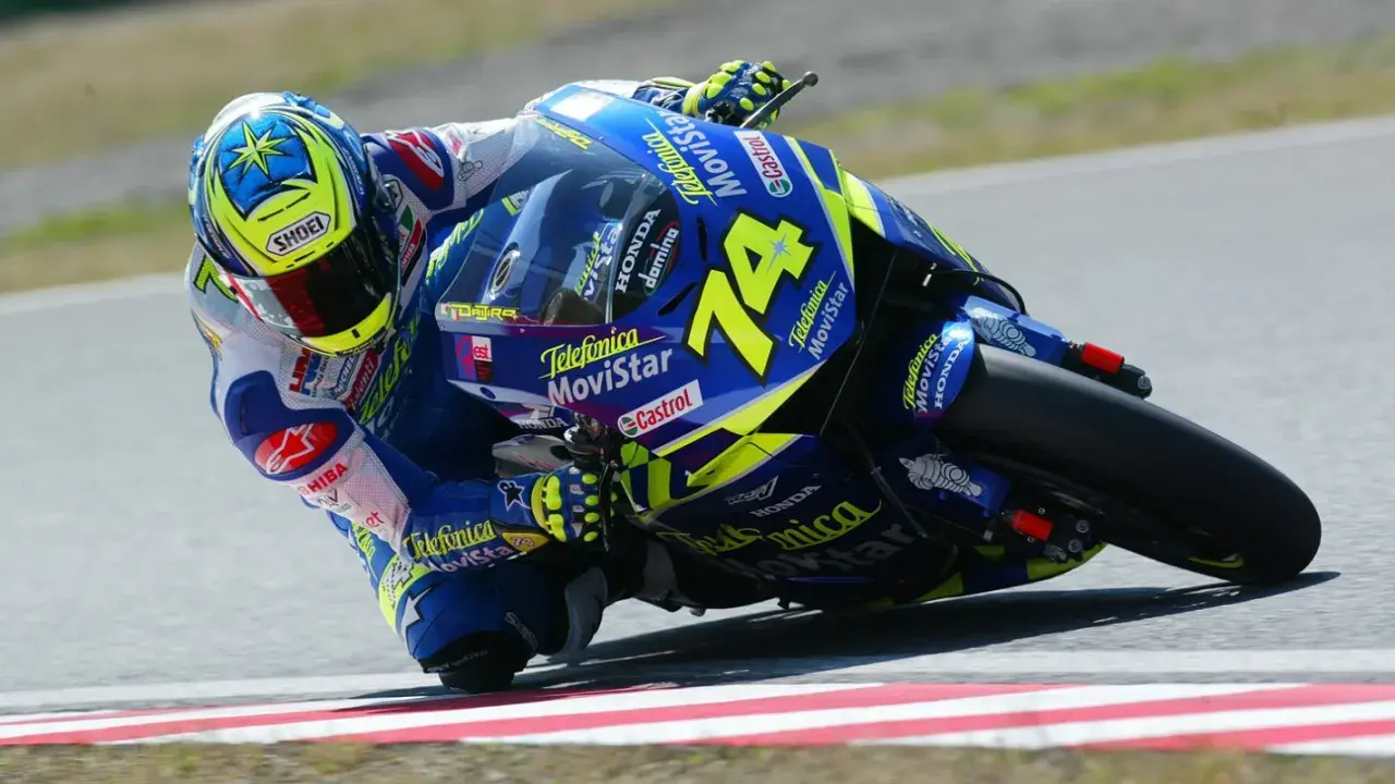 Daijiro Kato inclinado en su moto azul y amarilla, número 74, en una curva cerrada.