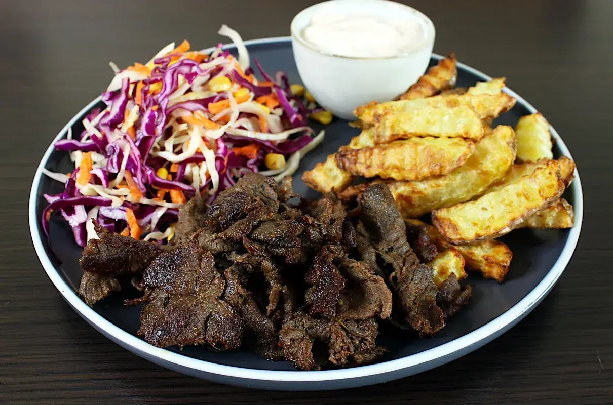 Talerz z mięsem kebab, frytkami, surówką z czerwonej kapusty i sosem.