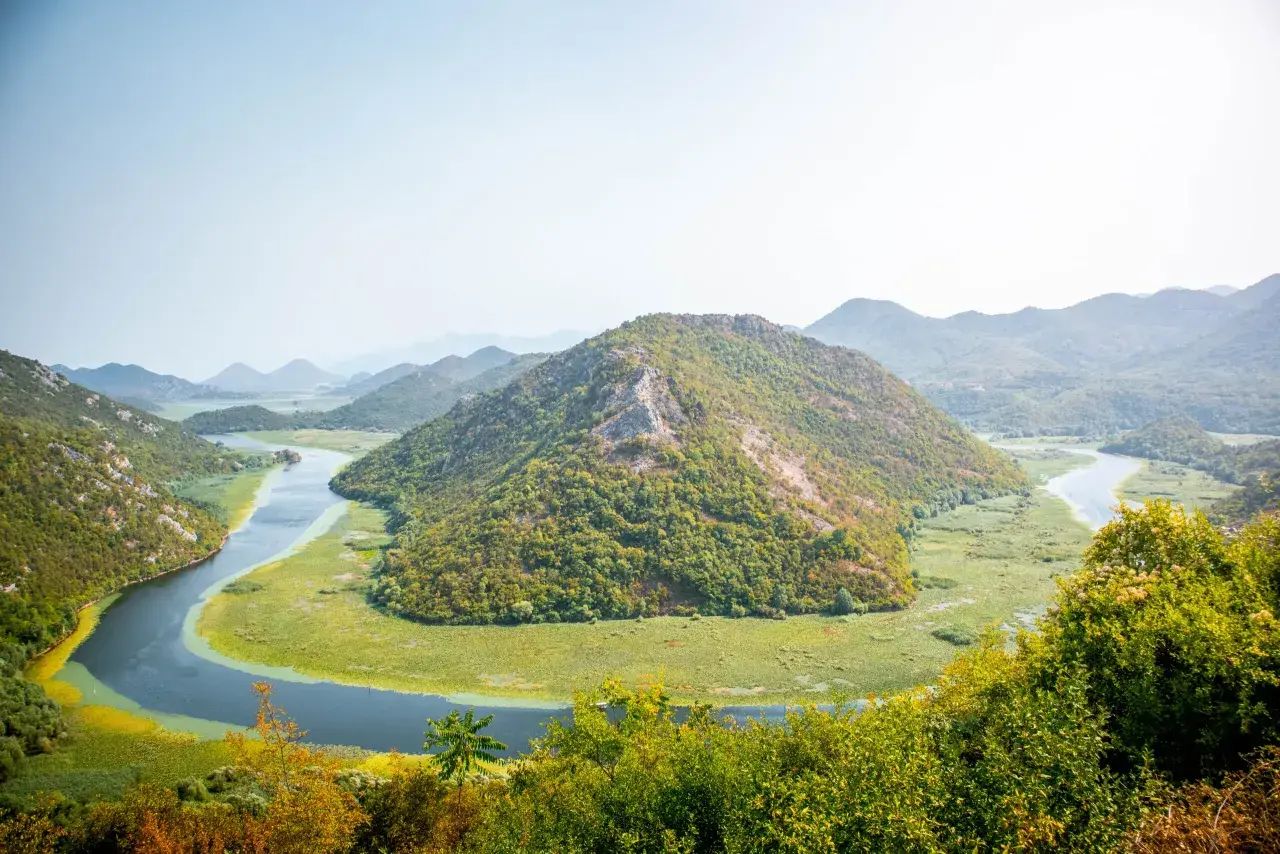 A winding river snakes through lush green hills and a vast wetland, a perfect scene for planning how many days in Montenegro.