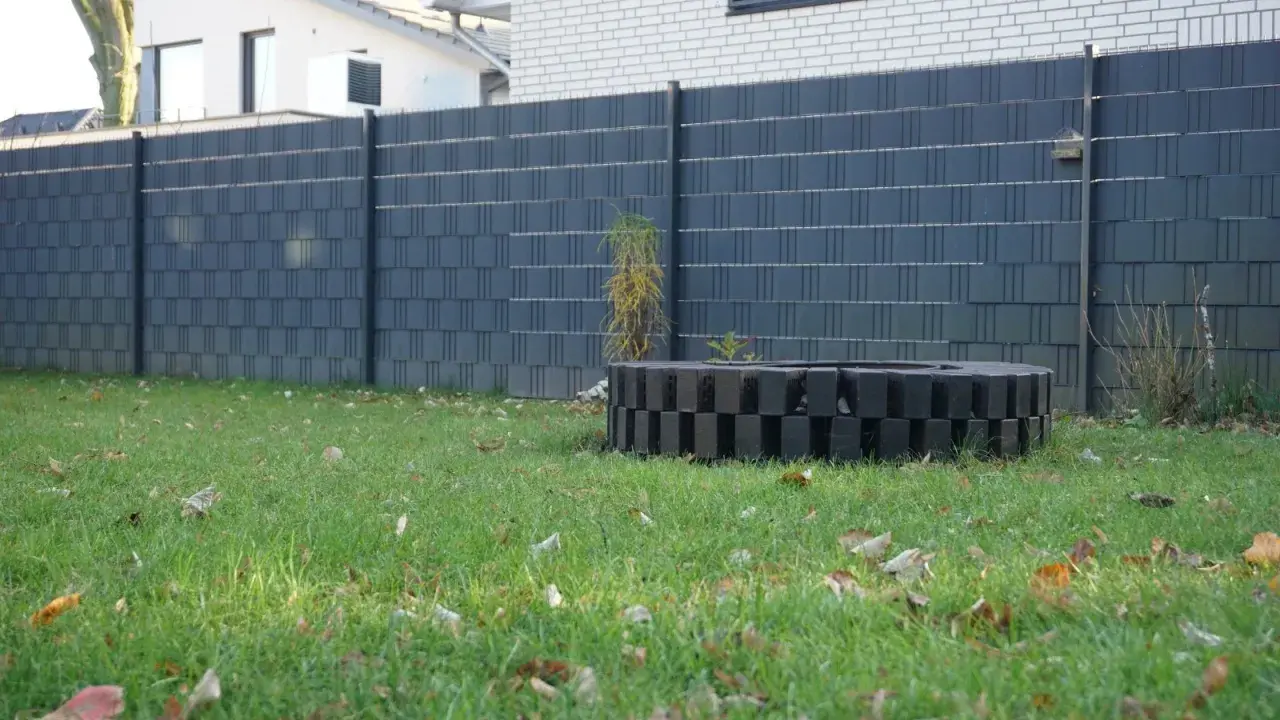 Moderne Zaun-Sichtschutz-Ideen: Dunkelgrauer Lamellenzaun mit dekorativem Feuerring im Garten.