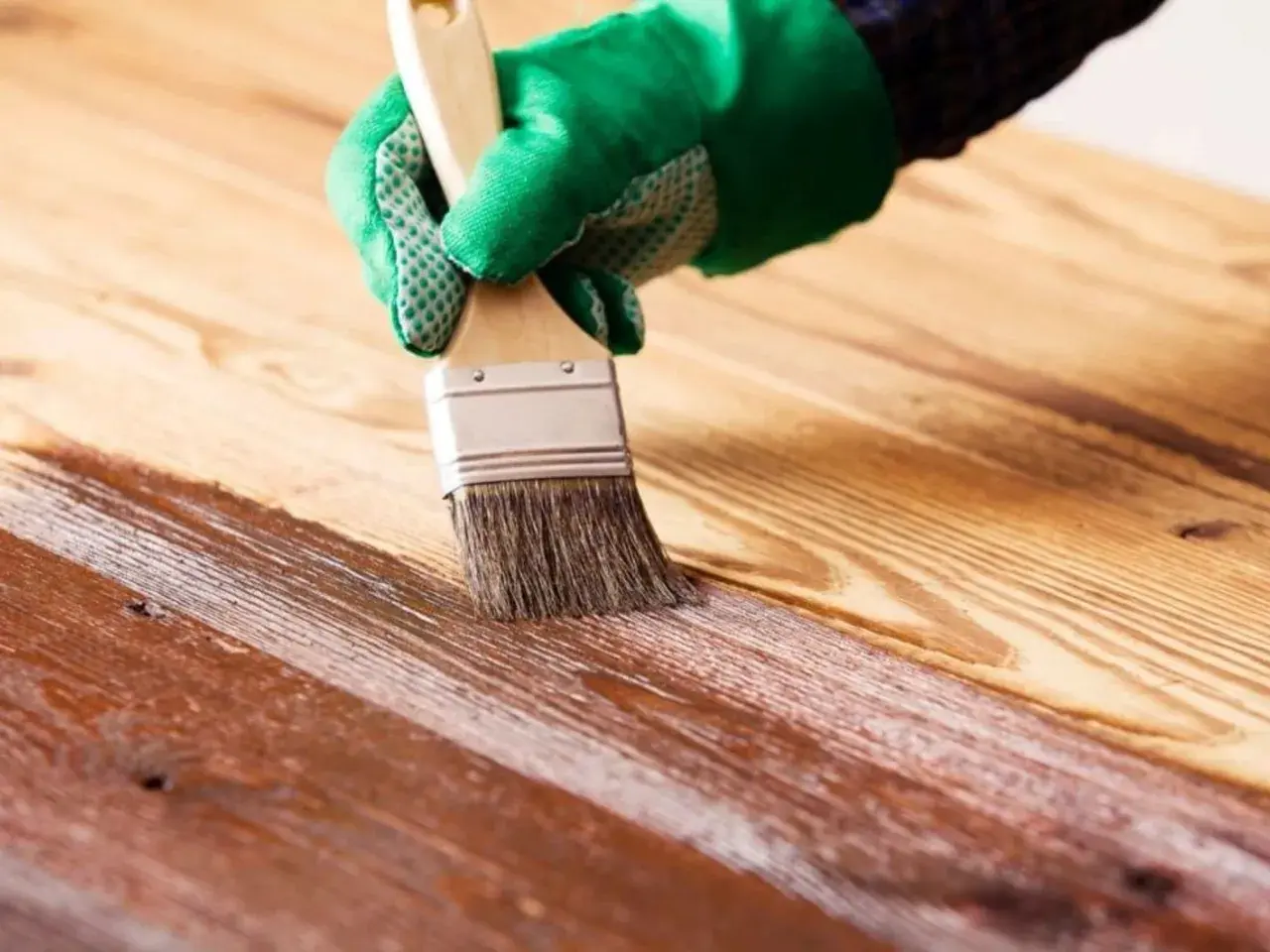 Mano con guante verde aplicando barniz a madera. Proceso para saber como impermeabilizar madera y protegerla.
