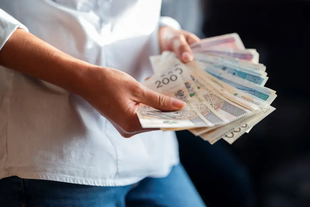 Ręce trzymające polskie banknoty. Zastanawiasz się, jaka będzie najniższa krajowa 2025 i ile na rękę dostaniesz?