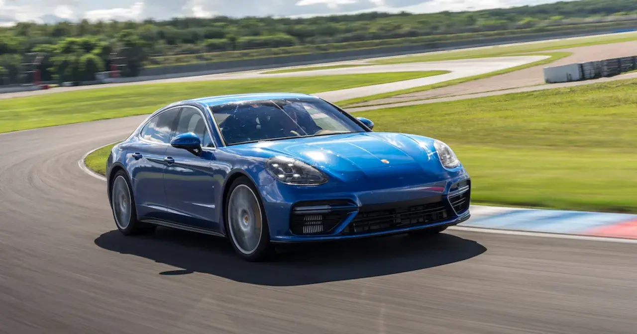 Niebieski Porsche Panamera GTS pokonuje zakręt na torze wyścigowym, z zielonymi wzgórzami w tle.
