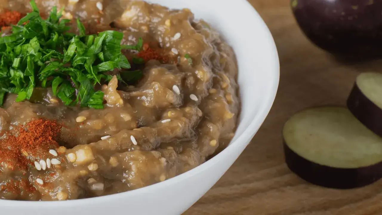 En krämig baba ganoush toppad med färsk persilja och paprikapulver. Bredvid syns skivade auberginer.