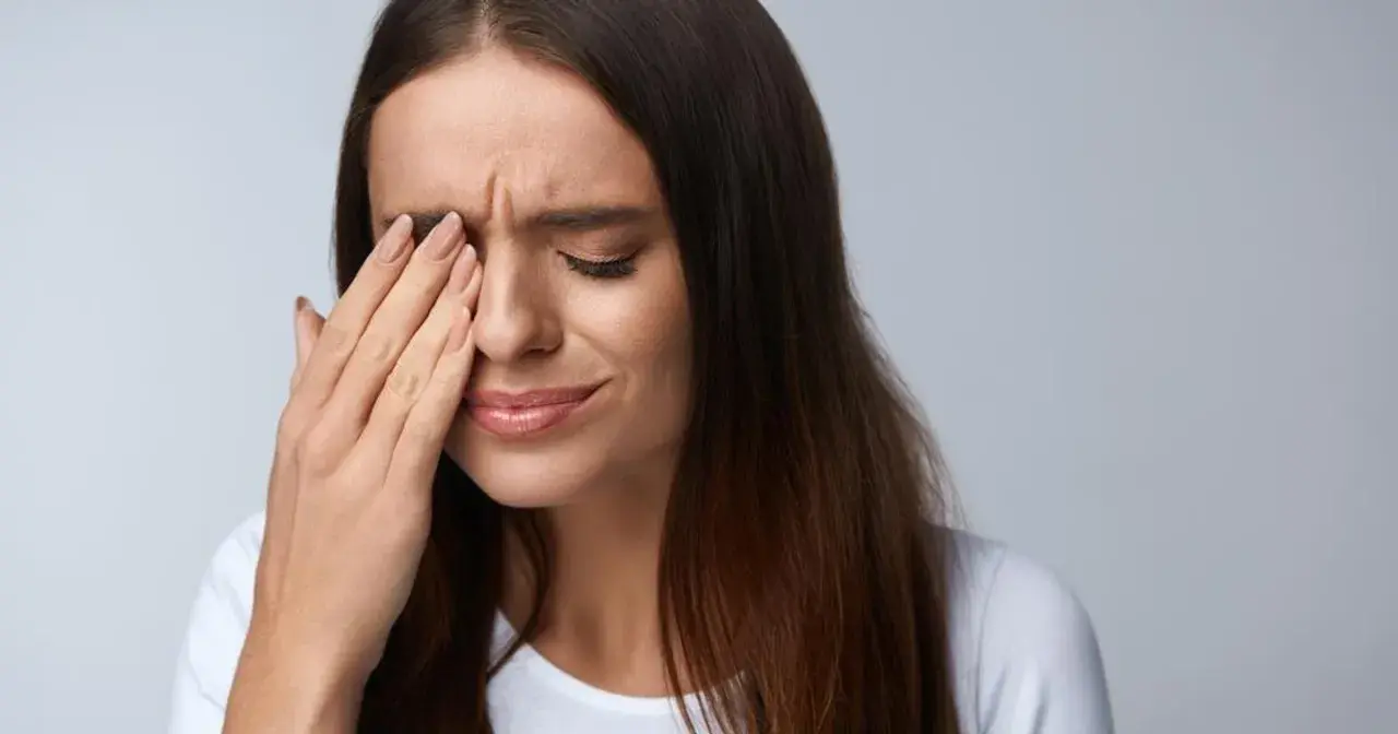 Kobieta zamyka oczy, pocierając je dłonią. Może to być jeden z objawów zespołu Sjogrena, który powoduje suchość oczu.