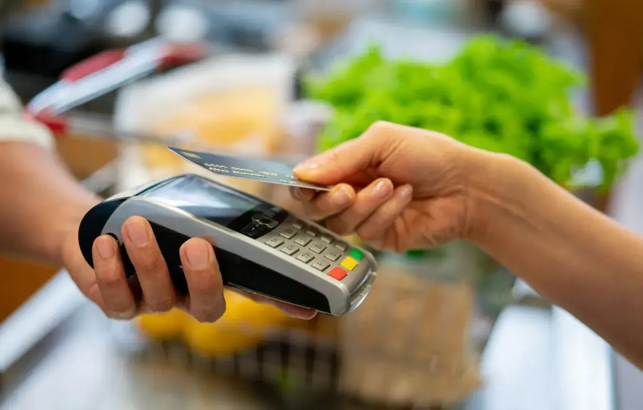 Une main approche une carte bancaire d'un terminal de paiement pour un paiement sans contact.
