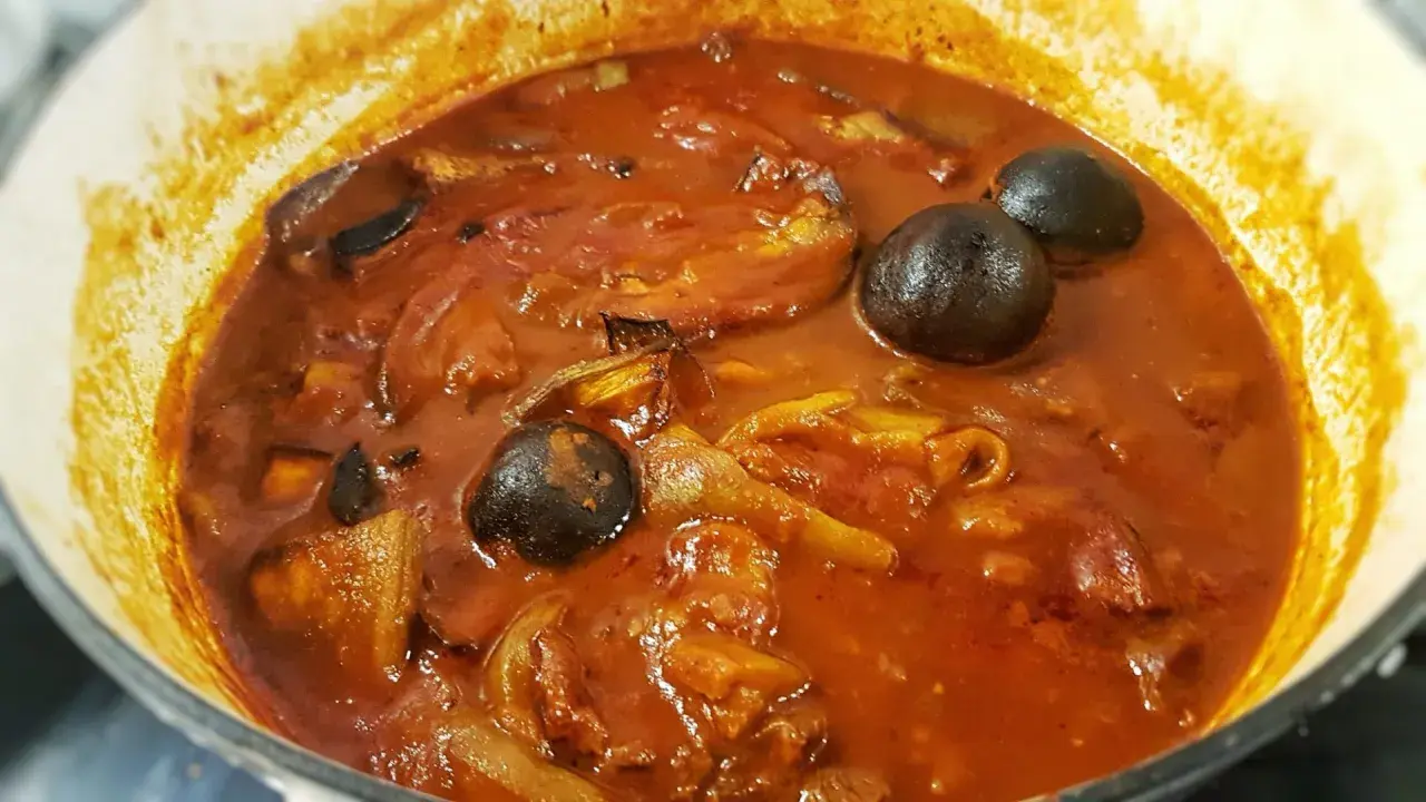 Khoresh Bademjan, a Persian eggplant stew, simmering in a pot with whole dried limes and chunks of eggplant.