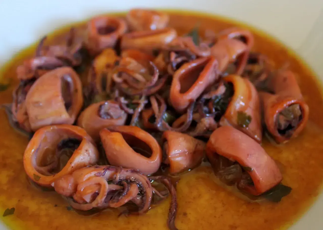 Calamares en salsa, tiernos y jugosos, con sus tentáculos enrollados, nadan en un rico caldo dorado.