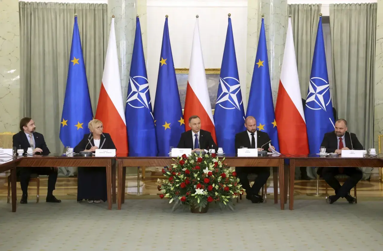 Spotkanie przy stole z flagami Polski, UE i NATO. Dyskusja o bezpieczeństwie i artykuł 5 NATO.