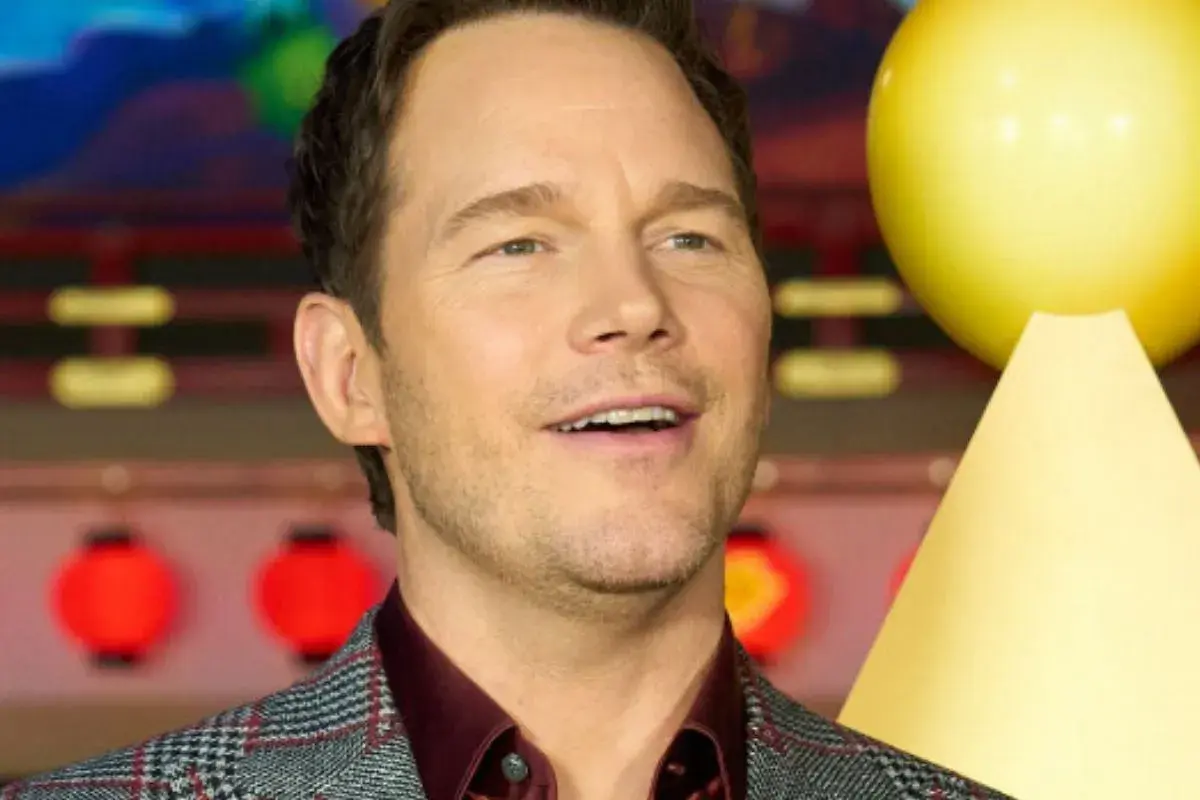 Chris Pratt, gwiazda wielu filmów, uśmiecha się na tle czerwonych lampionów i żółtej dekoracji.