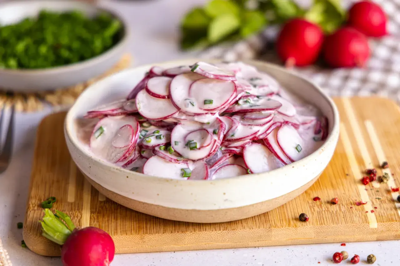 Frischer radieschensalat mit joghurt und schnittlauch, garniert mit pfefferkörnern.