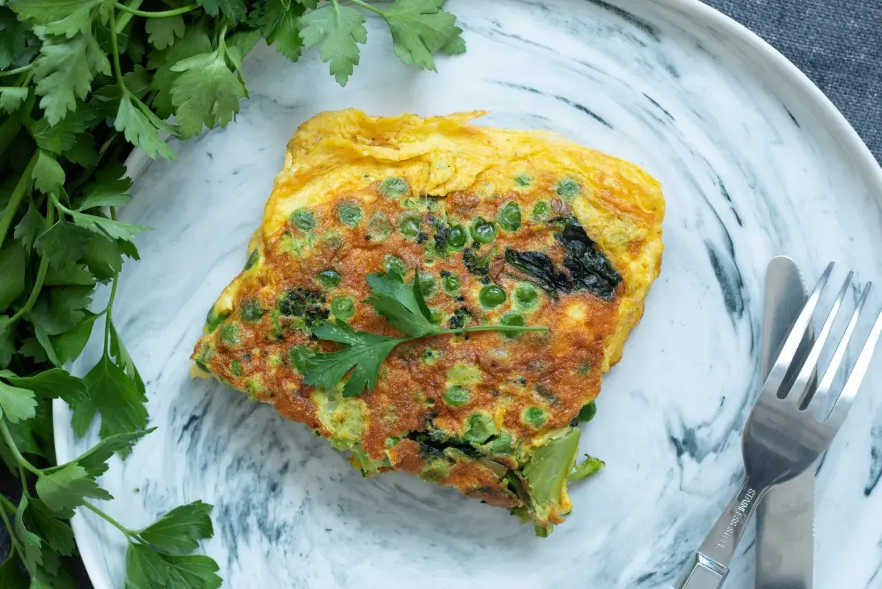 Une omelette aux petits pois et brocolis, garnie de persil frais. Une recette simple et savoureuse pour un repas léger.