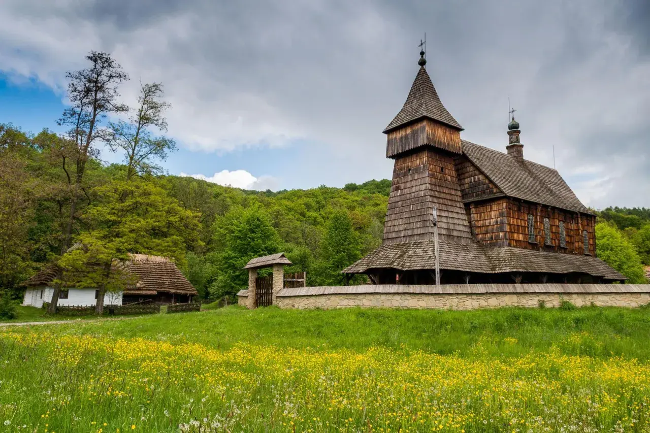 Drewniana cerkiew i chałupa na tle zielonych wzgórz. Największy skansen w Polsce zaprasza do podróży w czasie.