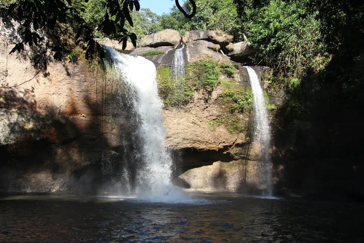 Zwei Wasserfälle stürzen in Khao Yai in einen dunklen Pool. Üppige Vegetation umgibt die Felsen.