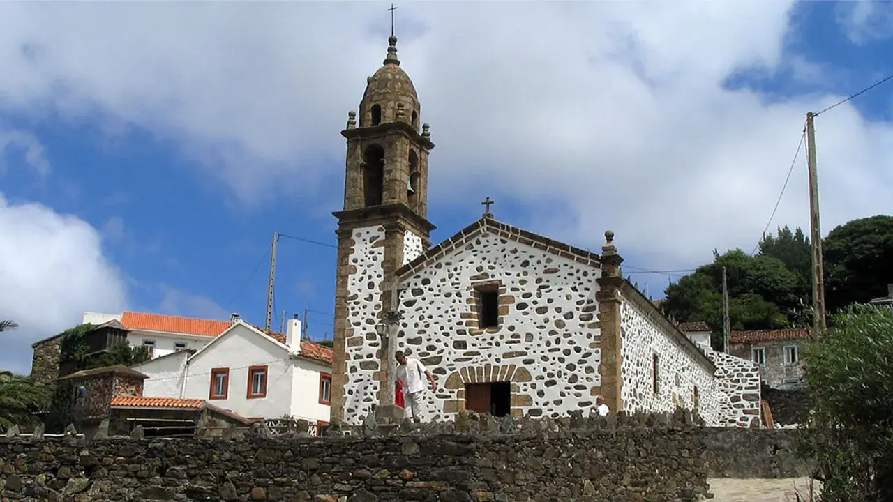 Iglesia de San Andrés de Teixido, con su campanario y fachada de piedra y cal, bajo un cielo nublado.