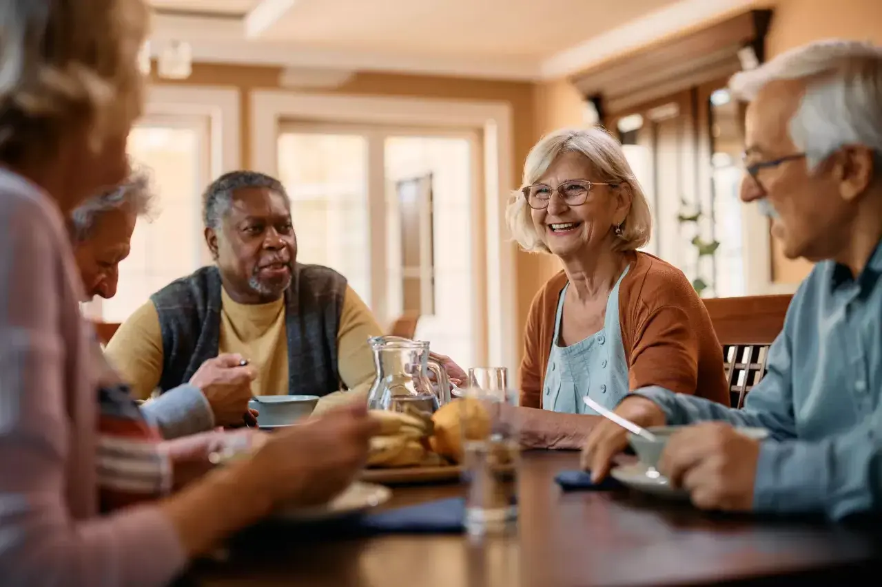 Des seniors joyeux partagent un repas, discutant de ce qu'est un cap retraite.