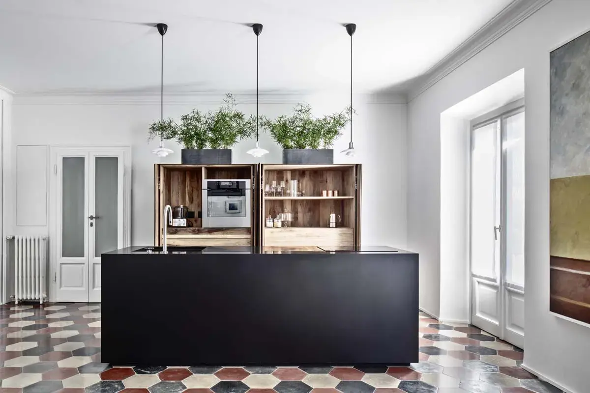 Cucina moderna con isola nera, pensili in legno, piante e pavimento con cementine esagonali colorate.