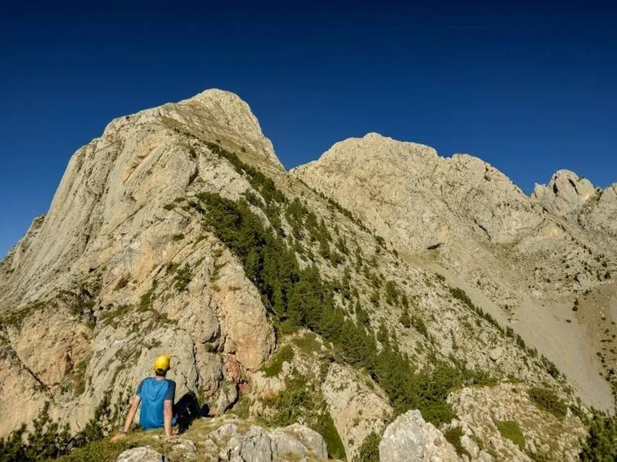 Un excursionista con casco amarillo contempla imponentes montañas, un paisaje ideal para rutas por Berga.