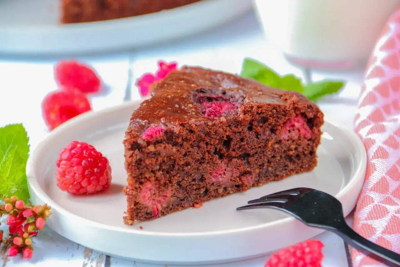 Tranche de gâteau au chocolat et framboise sans gluten, décorée de fruits frais et d'une touche de menthe.