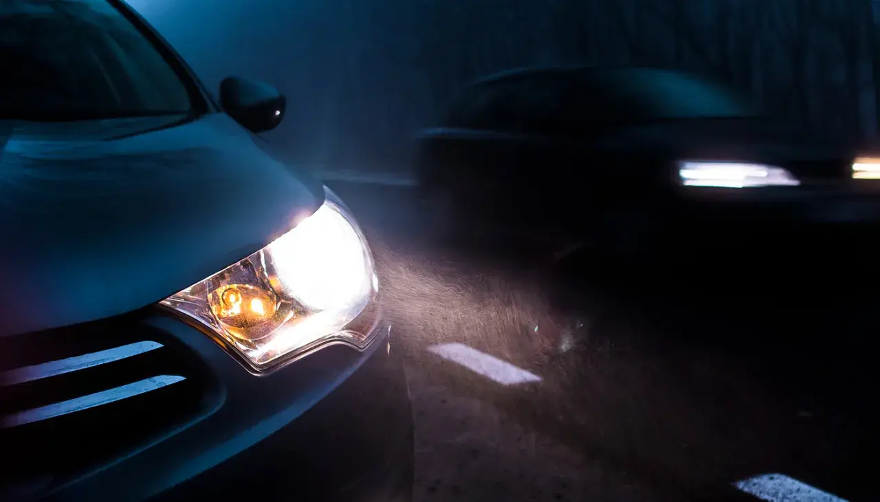 Mocna lampa led świeci jasno, rozświetlając mglistą noc i drogę. Inny samochód jedzie z przodu.